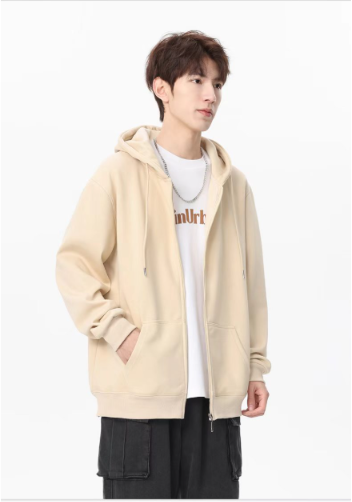 Front view of a young man showcasing a cozy cream beige zip-up hooded jacket with soft drawstrings layered over a white graphic tee and dark trousers.